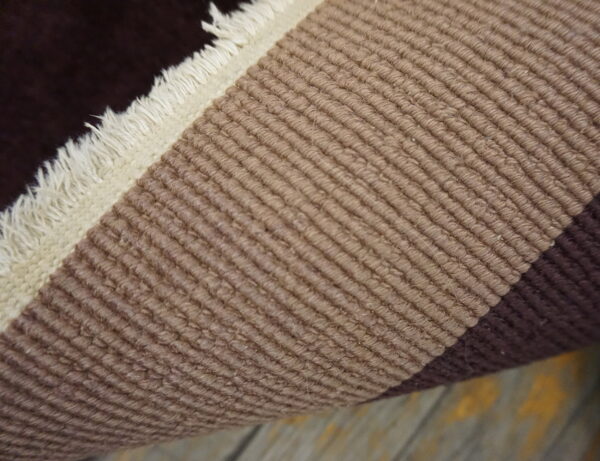 Rolled rug detail shows dark brown, cream fringe, and ribbed tan stripes on distressed wood floor.