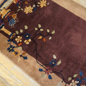 Burgundy pile rug with tan border and colorful floral motifs lying on light distressed wood planks.