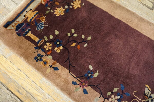 Burgundy pile rug with tan border and colorful floral motifs lying on light distressed wood planks.