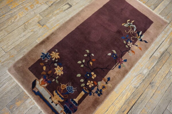 A deep maroon runner with a colorful floral pattern and tan border lies on distressed wood floors.