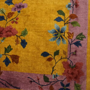Yellow rug with large red, blue, and purple floral patterns and a wide mauve border on wood flooring.