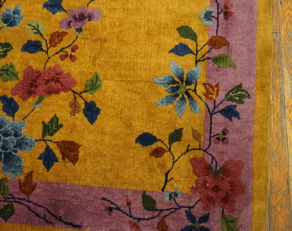 Yellow rug with large red, blue, and purple floral patterns and a wide mauve border on wood flooring.