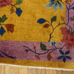 Floral rug in gold and mauve, bordered, resting on light brown wood flooring.
