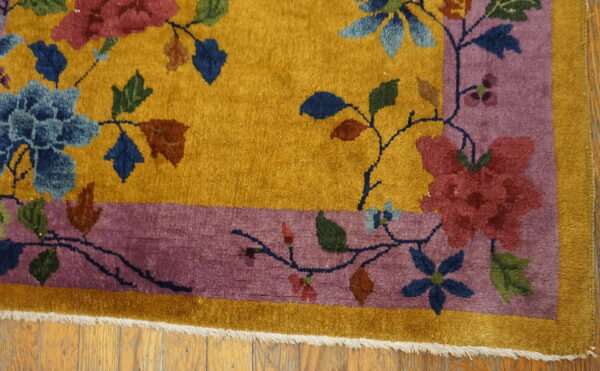 Floral rug in gold and mauve, bordered, resting on light brown wood flooring.