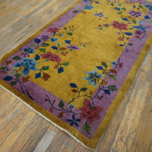 A mustard yellow rug with a purple border and colorful floral pattern rests on distressed hardwood floors.