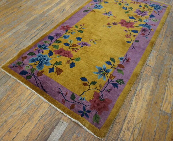 A mustard yellow rug with a purple border and colorful floral pattern rests on distressed hardwood floors.