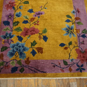 A golden yellow rug features colorful floral vines within a purple border on rustic wood flooring.
