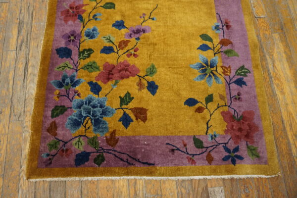 A golden yellow rug features colorful floral vines within a purple border on rustic wood flooring.