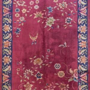 High pile berry rug with scattered multicolored flowers and a wide navy blue botanical border.
