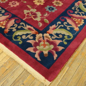 Close-up of a magenta and navy floral rug border resting on worn, light brown wood floorboards.