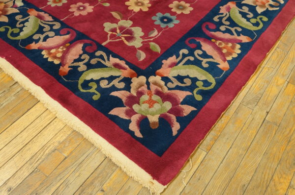 Close-up of a magenta and navy floral rug border resting on worn, light brown wood floorboards.