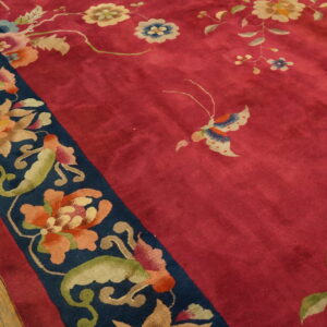 Close-up of a deep pink rug with multicolored floral border on a rustic wooden floor.