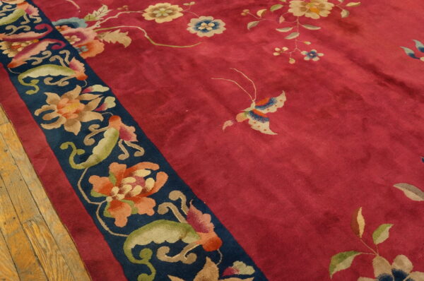 Close-up of a deep pink rug with multicolored floral border on a rustic wooden floor.