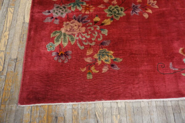 Crimson rug featuring multicolor floral patterns, bordered by fringe and set against distressed wooden planks.