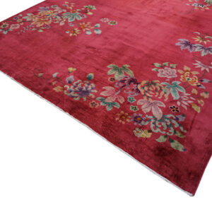 Deep magenta rug with scattered multicolor floral designs resting on distressed plank wood flooring.