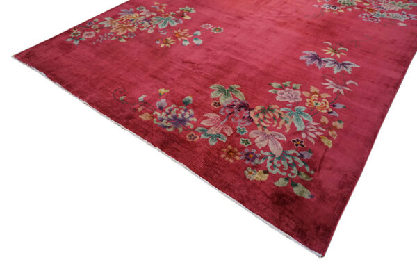 Deep magenta rug with scattered multicolor floral designs resting on distressed plank wood flooring.