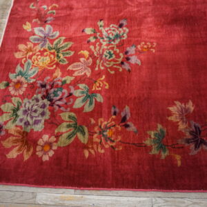 The shiny red rug features large multicolor floral motifs resting on distressed wooden plank flooring.