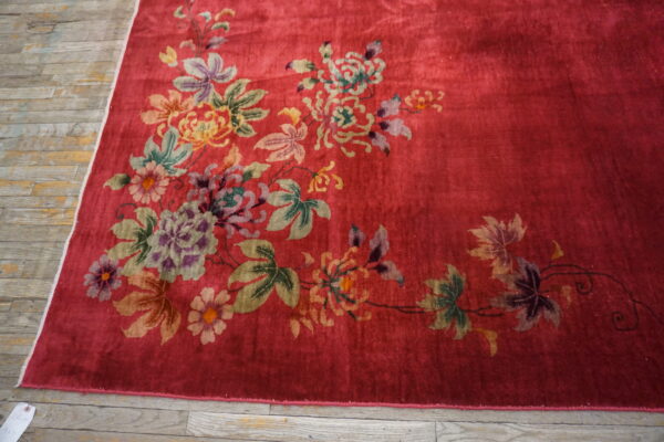 The shiny red rug features large multicolor floral motifs resting on distressed wooden plank flooring.