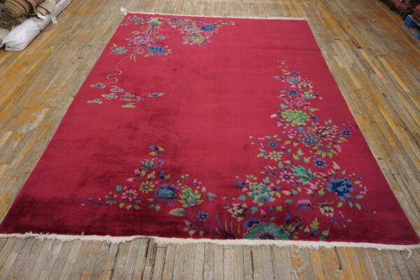 Bright magenta rug featuring sprawling multicolored floral designs lies on worn yellow wood flooring.
