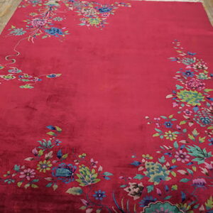 A velvety magenta rug with colorful floral corner designs lies on distressed wooden floorboards.