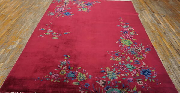 A velvety magenta rug with colorful floral corner designs lies on distressed wooden floorboards.