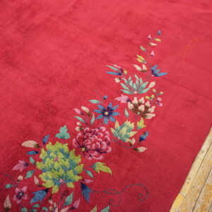 Crimson rug with a sweeping pattern of green, pink, and blue flowers resting on light wood planks.