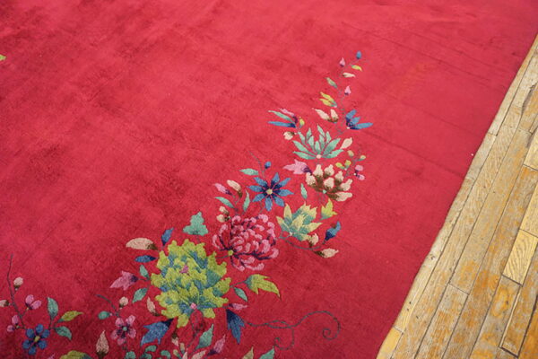 Crimson rug with a sweeping pattern of green, pink, and blue flowers resting on light wood planks.