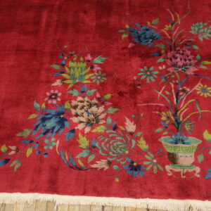 Red plush rug displaying large blue and green floral patterns rests on light wooden flooring.