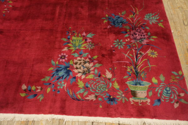 Red plush rug displaying large blue and green floral patterns rests on light wooden flooring.
