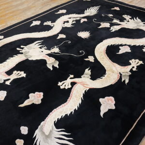 Plush black rug with pale dragon and cloud designs, resting on wide plank wood flooring.