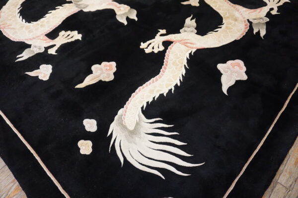 Black cut-pile rug featuring a large, detailed ivory and pink dragon and cloud pattern on wood flooring.