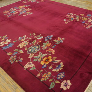 Low-pile crimson rug with colorful floral corner designs rests on worn wood planks.