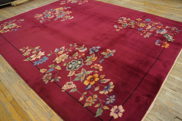 Low-pile crimson rug with colorful floral corner designs rests on worn wood planks.