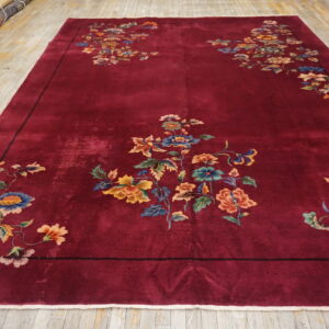 Burgundy rug with asymmetrical colorful floral and vine motifs on distressed light wood flooring.
