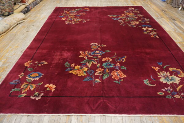 Burgundy rug with asymmetrical colorful floral and vine motifs on distressed light wood flooring.