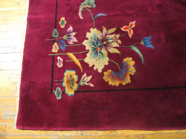Burgundy plush rug displaying a corner floral motif in teal, gold, and blue on distressed wooden flooring.