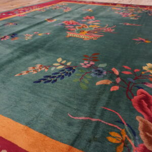 Close-up view of a lustrous teal rug featuring multicolored floral designs and a thick red and orange border.