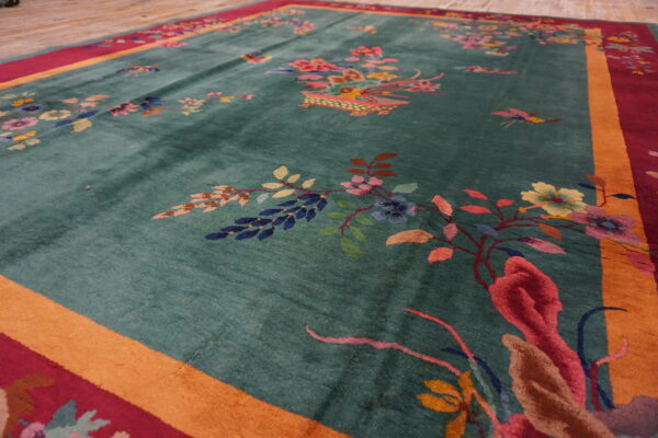 Close-up view of a lustrous teal rug featuring multicolored floral designs and a thick red and orange border.