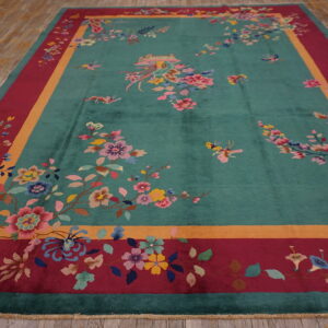 Large teal rug with elaborate floral designs, a gold stripe, and a deep red outer border on wood flooring.