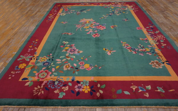 Large teal rug with elaborate floral designs, a gold stripe, and a deep red outer border on wood flooring.