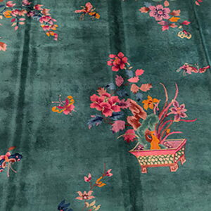 Greenish-blue rug with scattered pink and orange floral patterns, including a planter detail and magenta border.