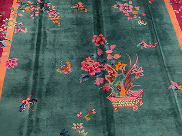 Greenish-blue rug with scattered pink and orange floral patterns, including a planter detail and magenta border.