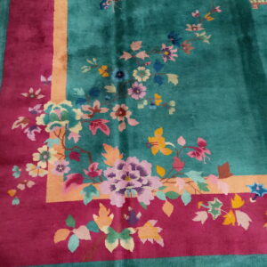 A teal rug featuring a multicolored floral design and a broad magenta and peach border on white tile.
