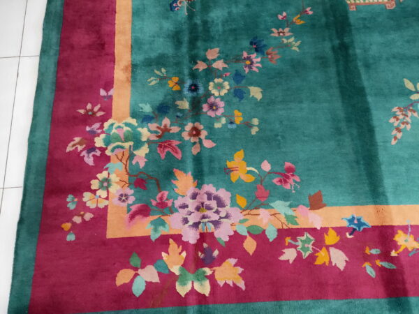 A teal rug featuring a multicolored floral design and a broad magenta and peach border on white tile.