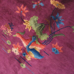 Textured purple rug detail showing colorful geese, blue and orange flowers, and green leaves.