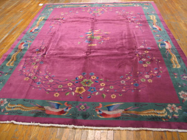Magenta rug featuring an ornate floral vine and exotic bird border resting on a shiny hardwood floor.