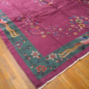 Magenta rug featuring floral vines and teal borders with colorful birds rests on worn wood plank flooring.
