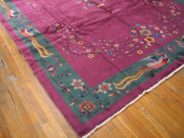 Magenta rug featuring floral vines and teal borders with colorful birds rests on worn wood plank flooring.