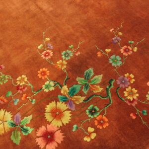 Close-up of a burnt orange rug featuring multicolored floral vines, leaves, and large stylized blooms.