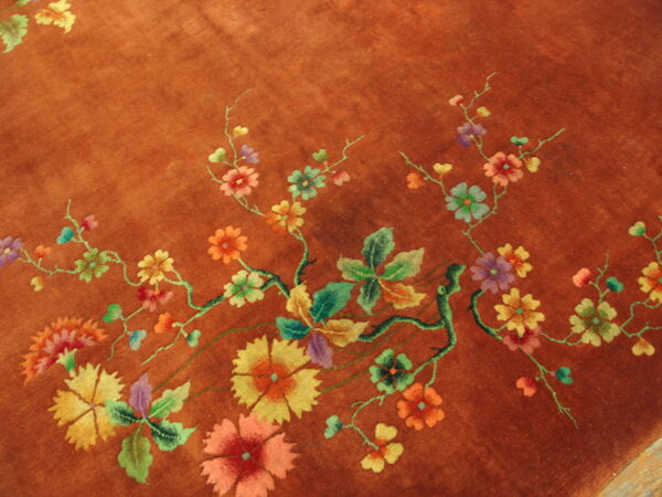 Close-up of a burnt orange rug featuring multicolored floral vines, leaves, and large stylized blooms.